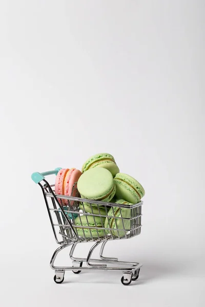 Montón de macarrones de color en un carrito de compras de juguete sobre fondo blanco — Foto de Stock