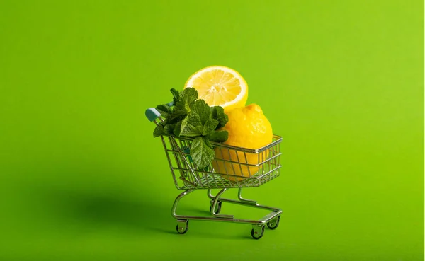 Limões e hortelã em um carrinho de brinquedo pequeno em um fundo verde. conceito de entrega loja online — Fotografia de Stock