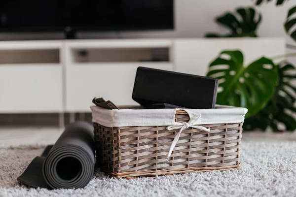 Yoga at home. gray yoga mat and black yoga blocks in a nice busket on the curpet in a white light living room. tv and monstera on a background — Stock Photo, Image