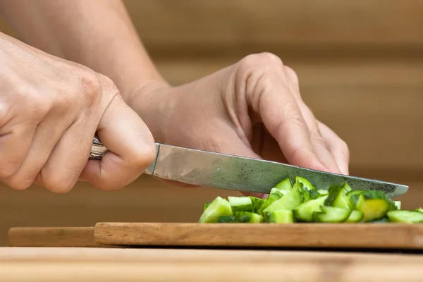 Manos rebanando pepino en la tabla de cortar de madera — Foto de Stock