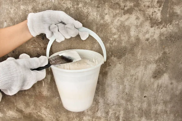 hands holding bucket with plaster and spatula