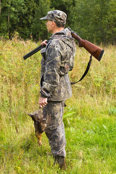 A hunter with a shotgun on his shoulder holds a downed game in h — Stock Image A hunter with a shotgun on his shoulder holds a downed game in h Royalty Free Stock Images