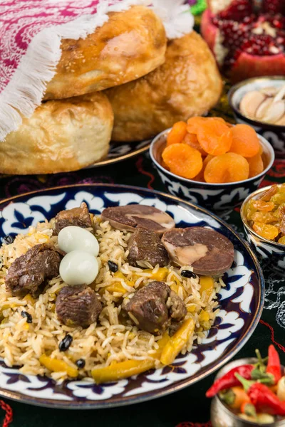 Traditional arabian gourmet. Pilaf with large pieces of fried halal meat, pieces of horse meat sausage, spicy rice, barberry, yellow carrots and quail eggs. On background dried apricots, red pepper, raisins, pomegranate.