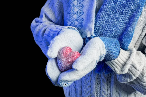 Hands in warm white gloves holding red heart on black background.