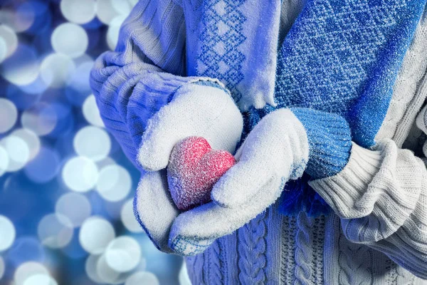 Hands in warm white gloves holding red heart on bokeh background.