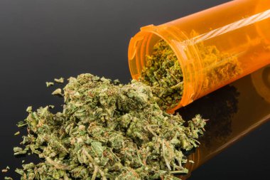 Tıbbi marihuanayı kapayın. Sarı hap şişesinde, siyah arka planda, ayna yansımalı.