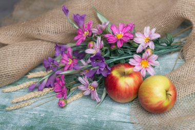 Yapay kozmos bipinnatus ve yeşil ahşap masada elmalar