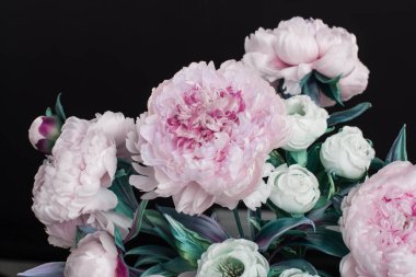 Dekorasyon yapay şakayıklar ve vazoda beyaz güller. Ahşap koltukta siyah arka planda.