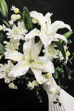 Siyah arkaplanda süslemeli vazo yapay zambaklar.