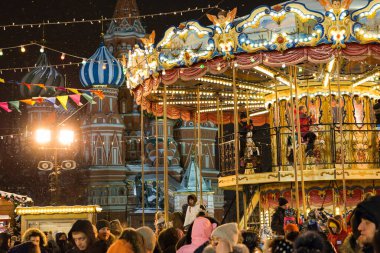 MOSCOW, RUSSIA - 5 HAZİRAN 2017: Moskova 'daki Kızıl Meydan' da Noel pazarında insanlar, Noel pazarında Atlıkarınca sallanıyor. St. Arka planda Basil Katedrali (kar fırtınası).