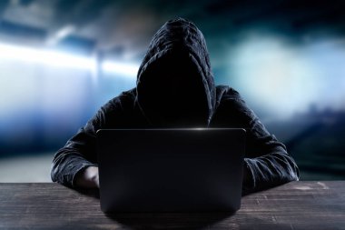 Bilgisayarının önünde bilgisayar korsanı. Koyu surat. Bulanık arkaplan