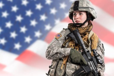 Amerikan Ordusu askerinde (ISAF) tüfekli bir kadın. Stüdyoda çekilmiş. Arka planda ABD bayrağı