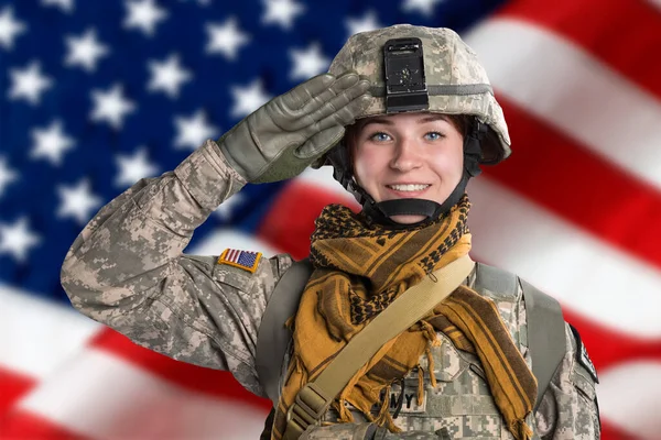 Female in USA Army soldier uniform saluting and smile look at the camera. Flag of USA on background