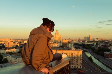 MOSCOW, Rusya - 13 Haziran 2016: Yüksek çatının kenarında oturan genç ve cesur adam. Moskova 'da yaz mevsiminde şafak vakti