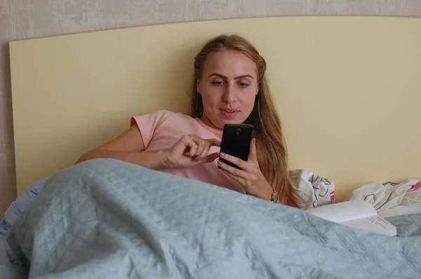 Young woman lies in bed and works with phone.