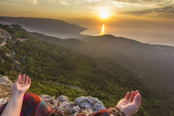 Hands of sitting girl in yellow mountain sunrise above sea — Stock Photo, Image