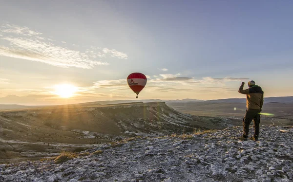 Воздушные шары на восходе солнца возле большой белой скалы — стоковое фото