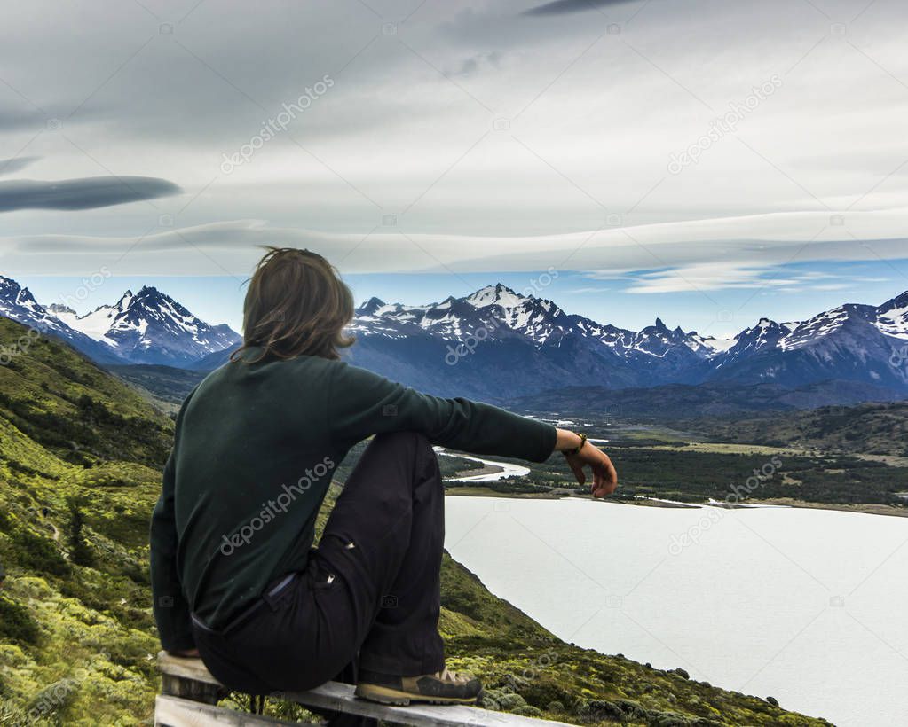 man sitting above lake in patagonia with grey sky