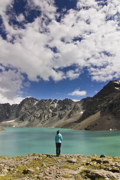 Chica en chaqueta azul de pie sobre el lago azul con montañas rodeadas — Foto de Stock