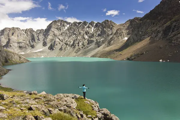 Ragazza in giacca blu in piedi con hands-up sopra il lago blu in montagna — Foto Stock