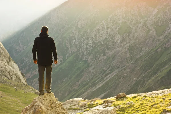 Mann in schwarzer Jacke steht mit erhobenen Händen auf Stein über den Bergen bei Sonnenuntergang — Stockfoto