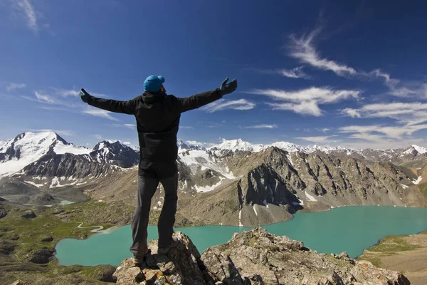 Man in black jacket standing with hands-up above blue lake in mountains — Stock Photo, Image