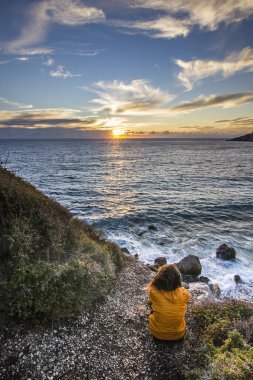 Sarı ceket günbatımında sahil oturan kız