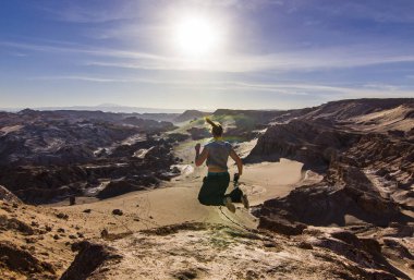 Kız atacama Çölü'nde tuzlu ayın Vadisi'nde bir uçurumun üzerinde günbatımında atlama