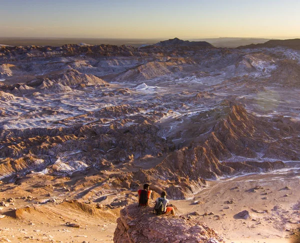 Человек, сидящий на скале в соленой лунной долине в пустыне атакама на закате — стоковое фото