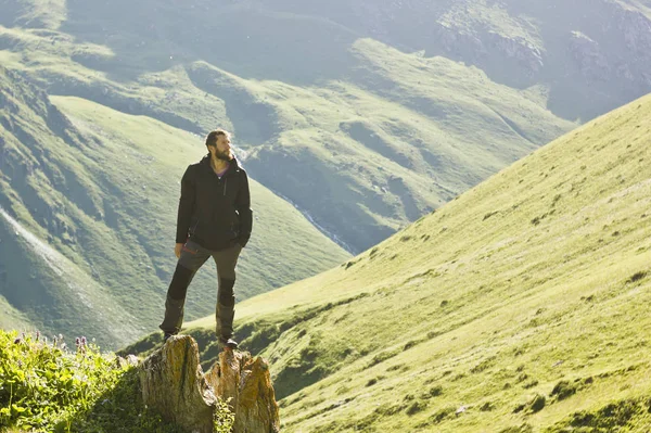 Hombre de chaqueta negra de pie sobre piedra con las manos arriba por encima de mountais al atardecer — Foto de Stock