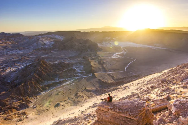 Hombre sentado en un acantilado en el salado valle de la Luna en el desierto de atacama al atardecer — Foto de Stock