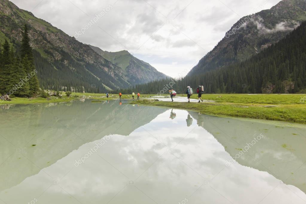 tourists hiking in green mountains with mirror of lake