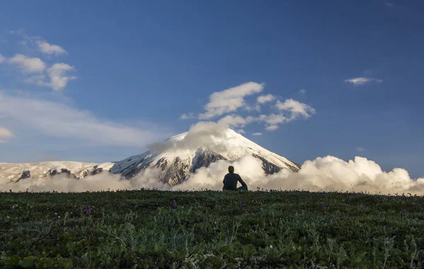 Hombre sentado en el campo cerca de volcanes activos de Kamchatka con colinas nevadas — Foto de Stock