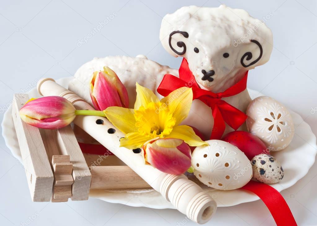 Traditional Czech easter decoration - white lamb cake with tulips and daffodil, lacy white eggs, flute and regional ratchet.