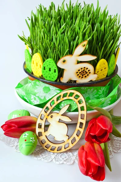 Traditional Czech easter decoration - green wheat seedings in the flowerpot and eggs with bunny decoration and red tulips on the white background. Spring easter holiday arrangement.