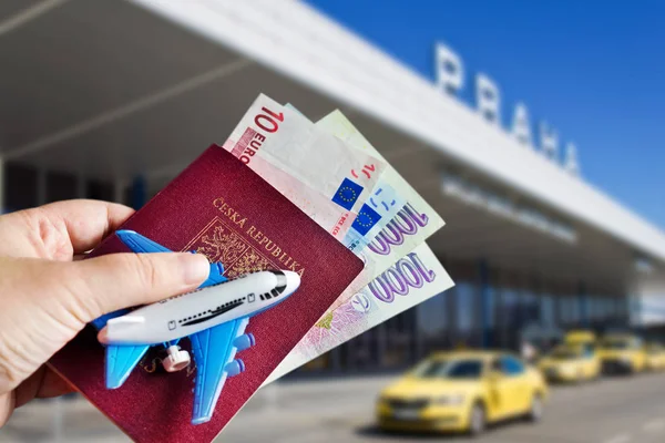 Hand with passport and money with model of plane on Vaclav Havel International airport, Ruzyne, Czech republic — Stock Photo, Image