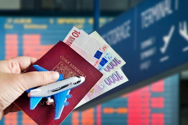 Hand with passport and money with model of plane on Vaclav Havel International airport, Ruzyne, Czech republic — Stock Photo, Image