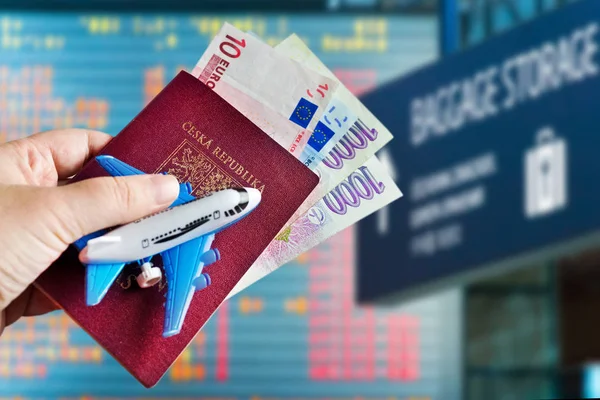 Hand with passport and money with model of plane on Vaclav Havel International airport, Ruzyne, Czech republic — Stock Photo, Image