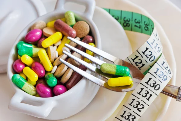 health care and wellness - diet pills and loosing weight - various tablets in a pot with measuring meter and forks
