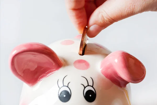 Economy and finance - savings in a money box - piggy bank and hand with coin — Stock Photo, Image