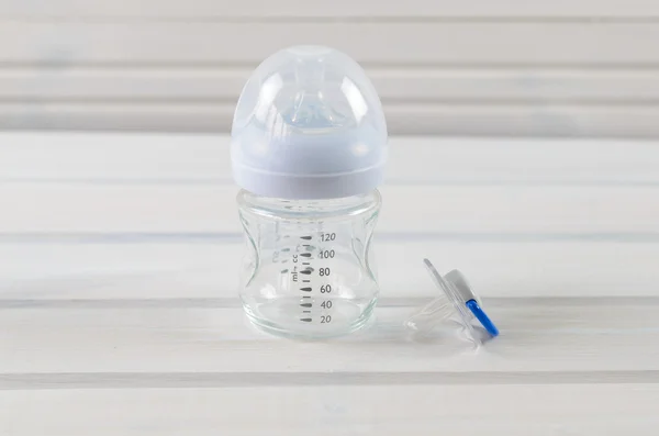 Glass baby bottle and baby pacifier on white wooden background — Stock fotografie