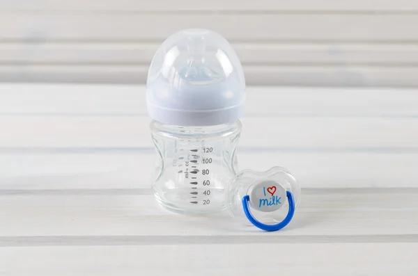 Скляна дитяча пляшка та дитячий соску на білому дерев'яному фоні — стокове фото