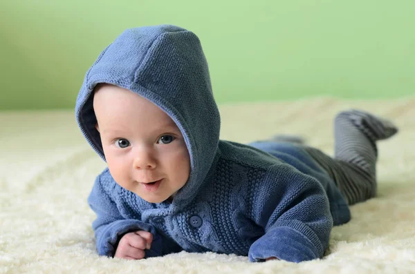Little boy in blue knitted cardigan lying on stomach and looking — Stock Photo, Image