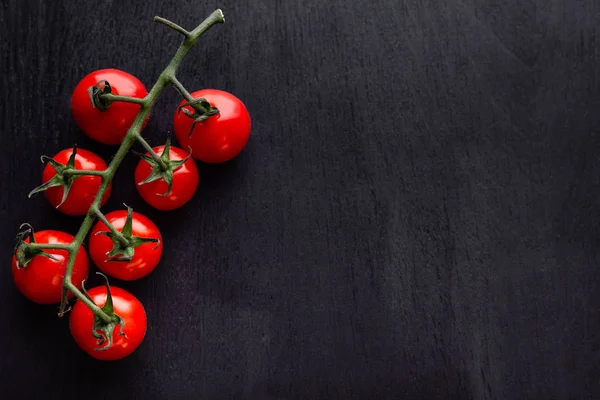 Cherry tomatoes on a black wooden table. Copy space. Background for cafe, menu, cookbook for recipes, restaurant.