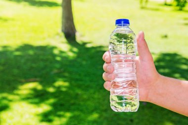 Cleardrinking su yeşil çim yaz arka plan üzerinde bir plastik şişe tutan adam