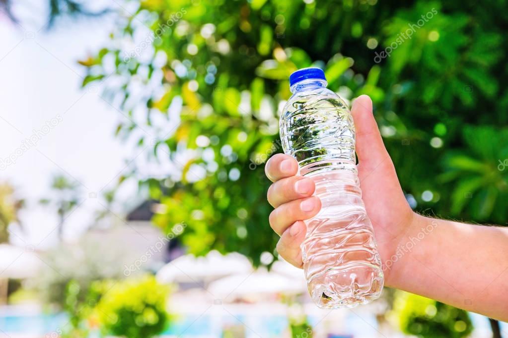 Man holding  clear drinking water in a plastic bottle on a summer blurred background