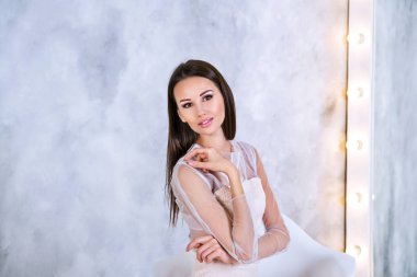 Kameraya bakarak gri arka plan ayna önünde oturan düz ve ipeksi saçlı genç esmer kadın