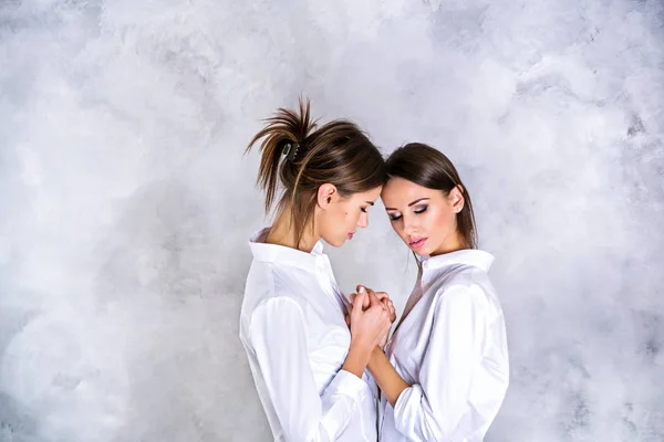 Two young brunette sisters in white shirts holding hands — Stock Photo, Image