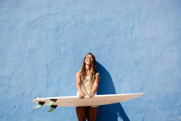 Glückliches Surfermädchen mit Surfbrett vor blauer Wand — Stockfoto