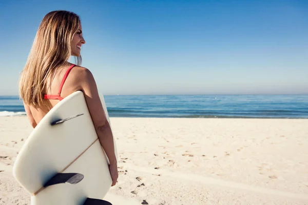 Jovem mulher carregando uma prancha de surf na praia . — Fotografia de Stock